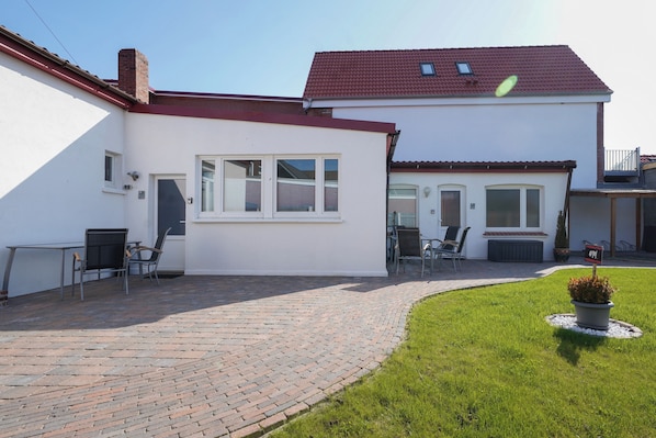 A two-story house with a red-tiled roof, a brick patio, and a small lawn area.