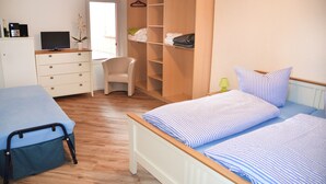 Un dormitorio con cama, una silla, armario, escritorio y televisor.