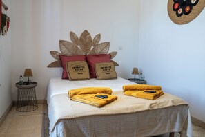 Ein ordentlich bezogenes Bett mit weißer Bettdecke, zwei roten Kissen und zwei gelben Handtüchern.