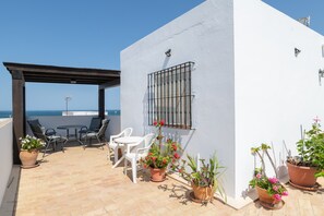 Eine Terrasse mit Gartenmöbeln, Blumentöpfen und Blick auf das Meer.