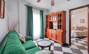 Een kamer met een groene bank, een houten kast met glazen deuren, een geruite vloer en een bed met beddengoed met een patroon.