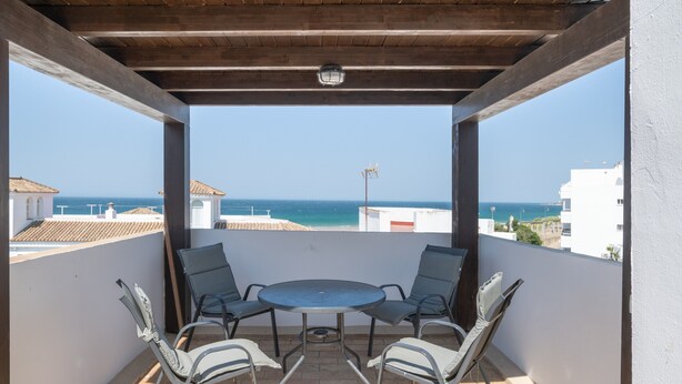 Un espace extérieur abrité, avec une table et des chaises, offrant une vue sur la côte.