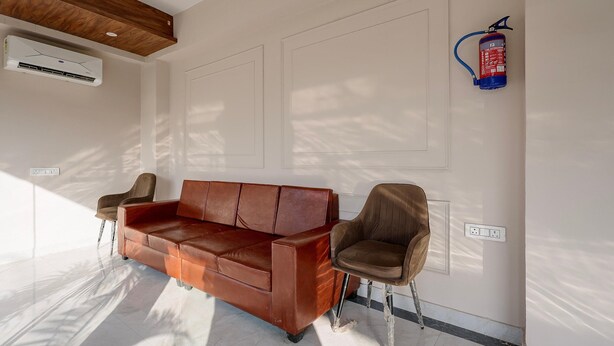 Una habitación moderna con un sofá de cuero marrón, dos sillones, un extintor de incendios montado en la pared y un equipo de aire acondicionado.