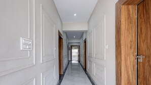 Un pasillo con paredes blancas, suelo de mármol y una puerta de madera a la derecha.