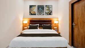 Una habitación de hotel con una cama, dos lámparas fijadas a la pared y una puerta de madera.