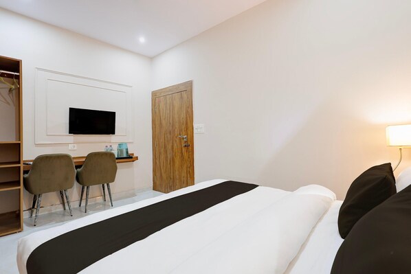 A hotel room with a bed, a desk with two chairs, a television mounted on the wall, and a wooden door.