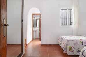 A bedroom with a bed, a window with bars, a door, and a bathroom visible through an archway. - Apartment 'Paqui Calle' with Private Terrace, Wi-Fi and Air Conditioning (Conil de la Frontera)