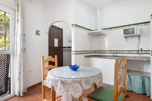 A compact kitchen with a round table, chairs, a microwave, and a small sink. - Apartment 'Paqui Calle' with Private Terrace, Wi-Fi and Air Conditioning (Conil de la Frontera)