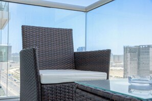 Ein Korbstuhl mit Kissen, ein Glastisch und Blick auf Gebäude durch ein großes Fenster.