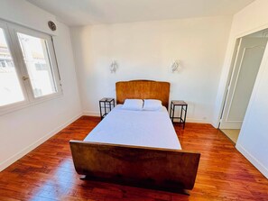 Une chambre à coucher avec un lit en bois, deux tables de chevet, une fenêtre et une porte.