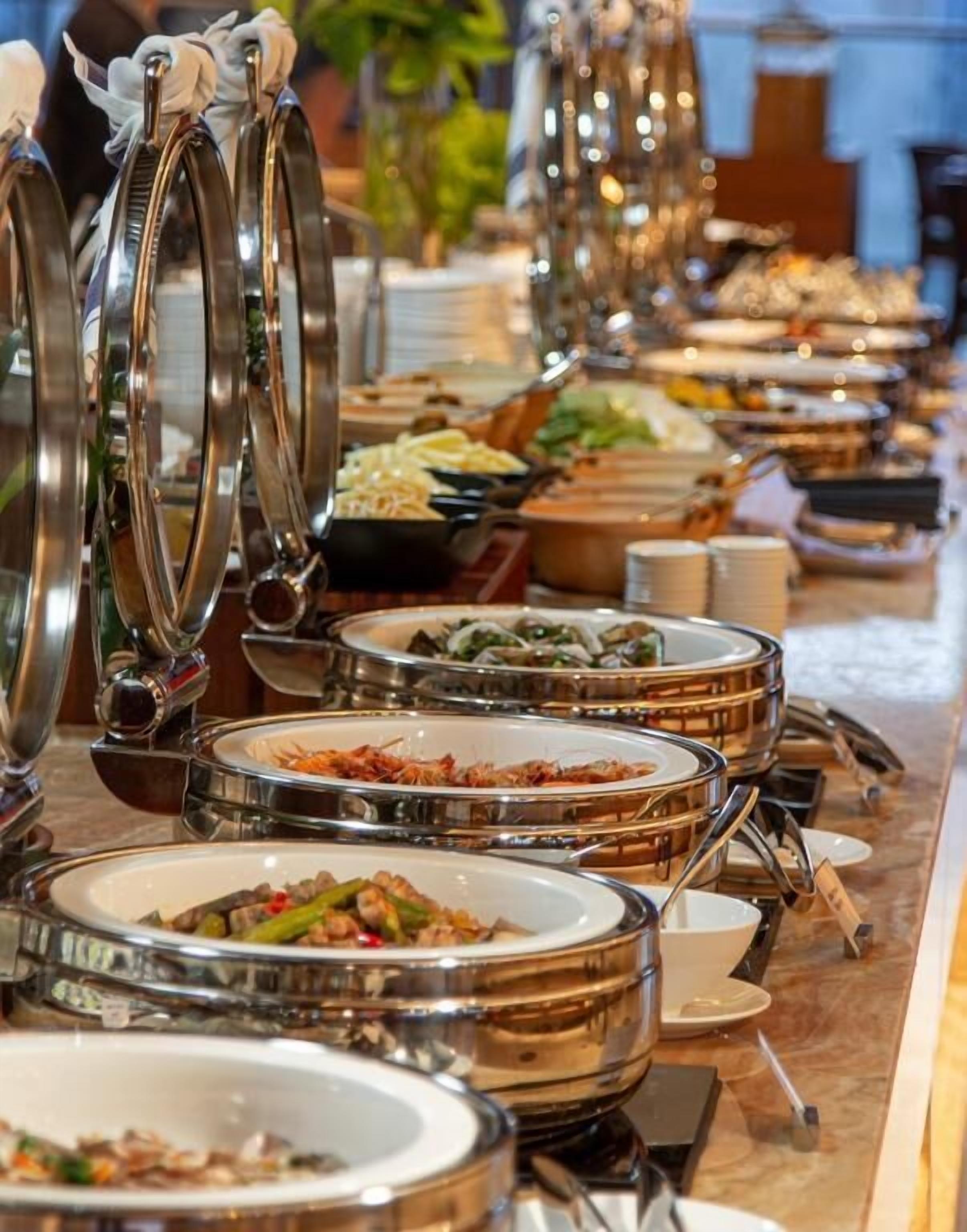 Buffet com várias estações de serviço, cada uma com bandeja de metal e variedade de pratos.