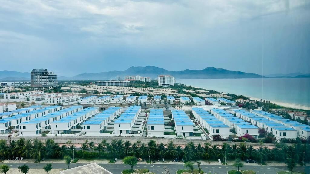 A coastal resort with multiple blue-roofed buildings, a marina, and mountains in the background.