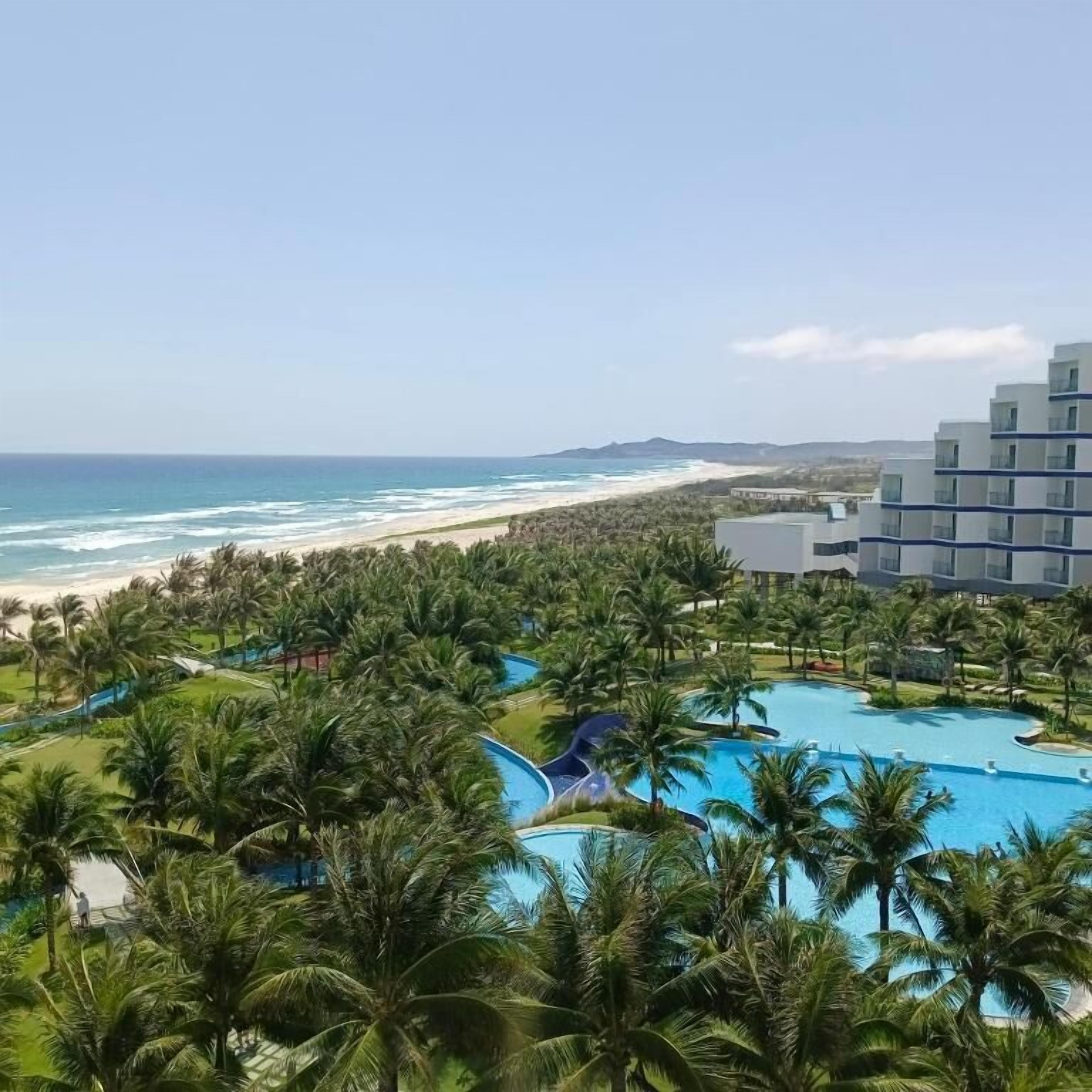 Un resort con piscina, palmeras y vista al mar.
