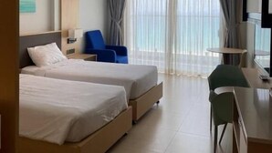 Habitación de hotel con dos camas, un escritorio, una silla, un televisor y un ventanal con cortinas.