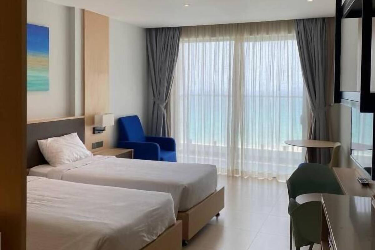 Habitación de hotel con dos camas, un escritorio, una silla, un televisor y un ventanal con cortinas.