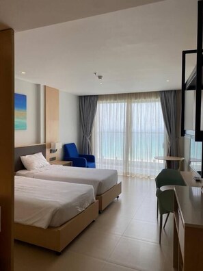 Habitación de hotel con dos camas, un escritorio, una silla, un televisor y un ventanal con cortinas.
