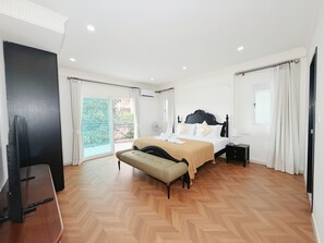 Een slaapkamer met een bed, een bankje, een televisie en een balkon.