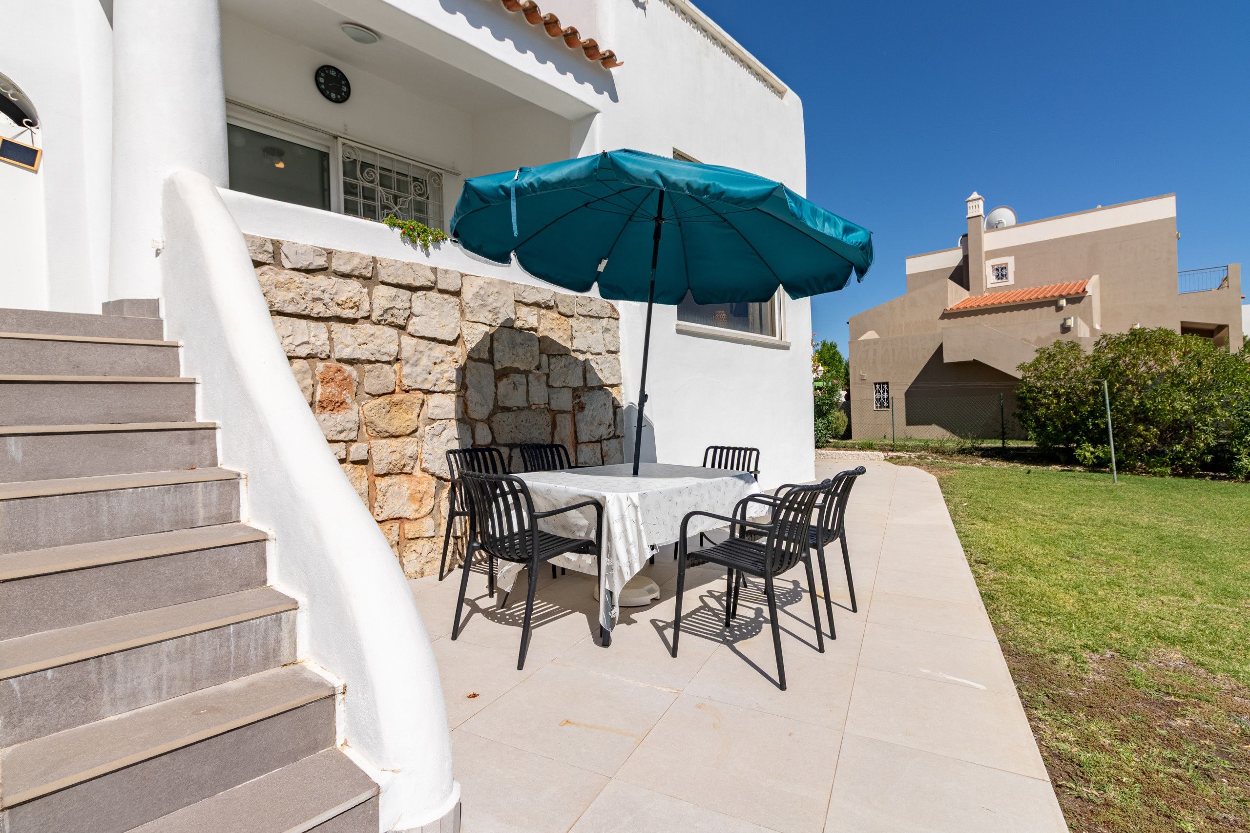 Une terrasse avec une table et des chaises, un mur en pierre et un parasol bleu.