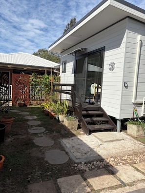 A single-story house with a front porch, a sliding glass door, and a small set of stairs leading to the entrance. - A cosy  cabin in Umina Beach (Umina Beach)