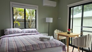 Quarto de hotel com cama, mesa e cadeiras, luminária e janelas amplas.