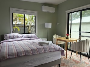 A hotel room with a bed, a table with chairs, a lamp, and large windows. - A cosy  cabin in Umina Beach (Umina Beach)