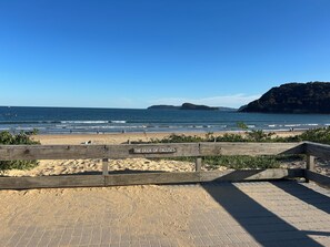 Una playa con una valla de madera que dice 'The Deck of Excuses', arena y el océano.