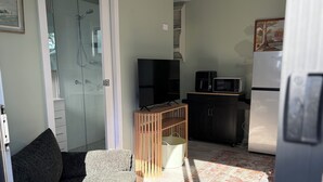 Um espaço compacto com sofá, televisão, micro-ondas, frigorífico, armário de madeira e área de chuveiro.