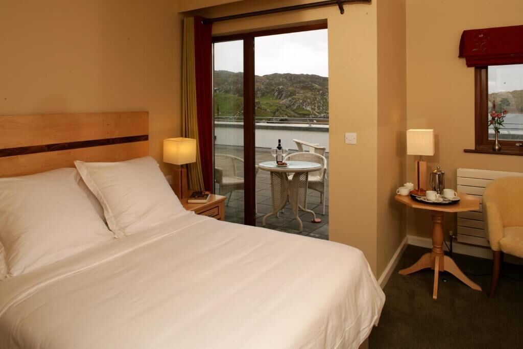 A hotel room with a bed, a small table with a lamp, a chair, and a view of the outdoors.