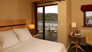 Una camera d'albergo con un letto, un tavolino con una lampada, una sedia e vista sull'esterno.