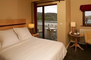 A hotel room with a bed, a small table with a lamp, a chair, and a view of the outdoors. - Inishbofin House Hotel (Inishbofin)