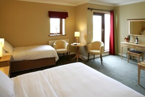 A hotel room with two beds, a desk, a chair, a lamp, and a window with curtains. - Inishbofin House Hotel (Inishbofin)
