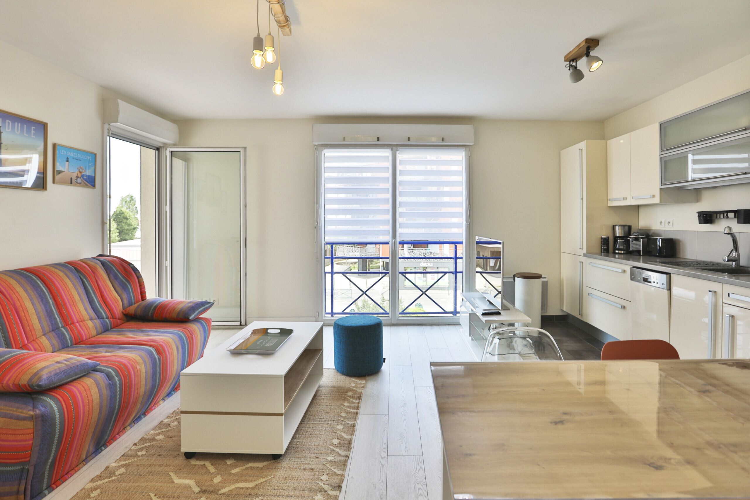 A modern apartment with a sofa, dining table, kitchenette, and a balcony with a view.