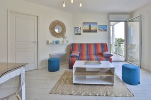 Ein Wohnzimmer mit Sofa, Couchtisch, blauem Hocker, Spiegel und Kunstwerken an der Wand.