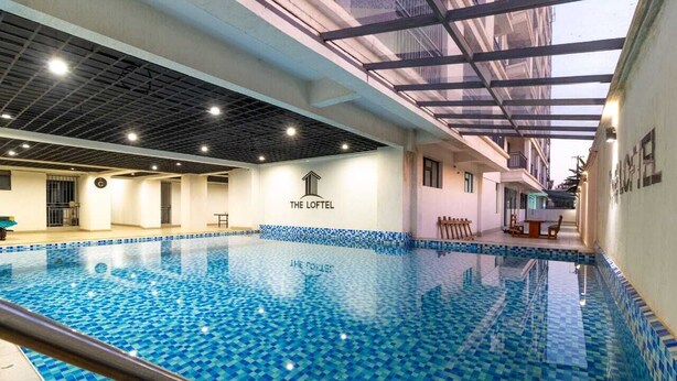 Una piscina interior con suelo de baldosas y techo de vigas a la vista.