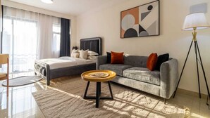 Una habitación de hotel moderna con una cama, un sofá gris, una mesita redonda pequeña, una lámpara de pie y un cuadro abstracto grande en la pared.