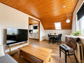 Ein moderner Loft-Wohnraum mit Holzbalkendecke, einem Fernseher, einem Essbereich und einer gemütlichen Sitzecke.