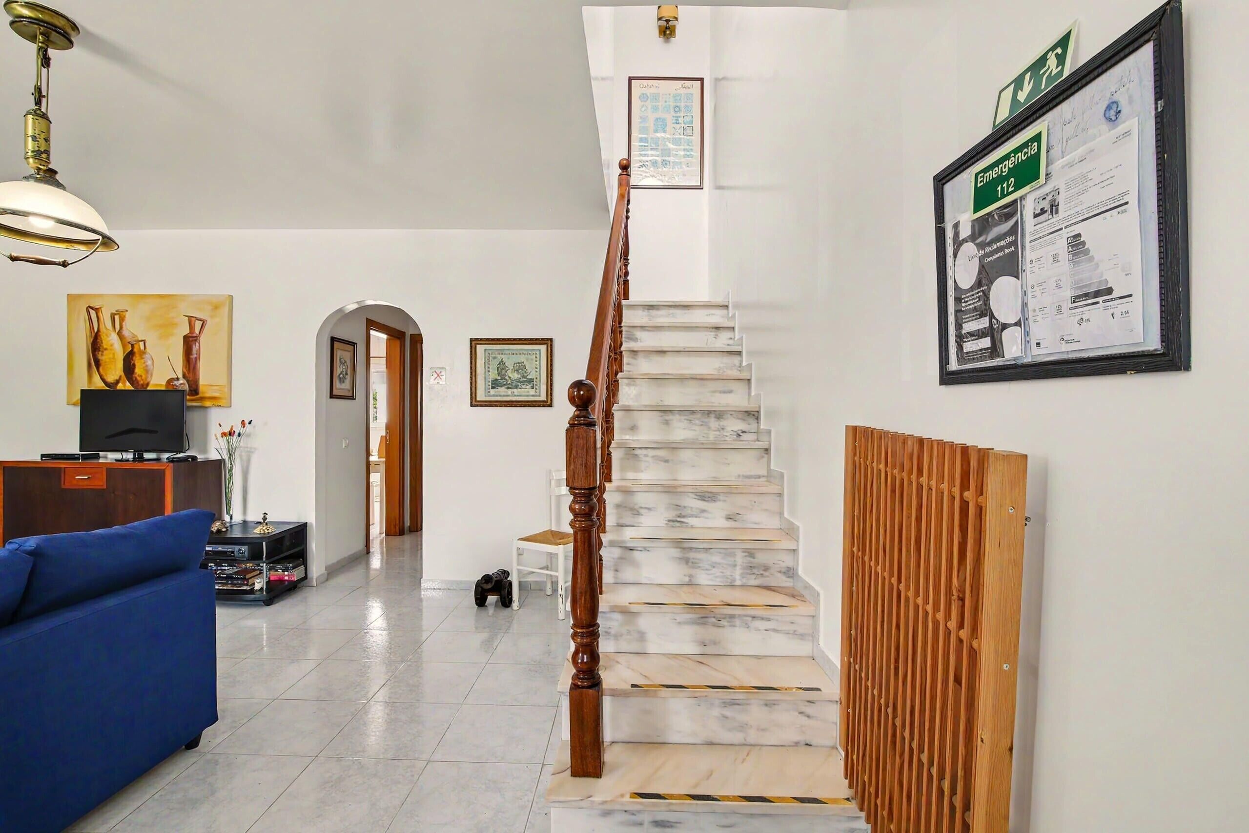 Una escalera con barandilla de madera, un cartel de salida de emergencia enmarcado y un cartel informativo en la pared.