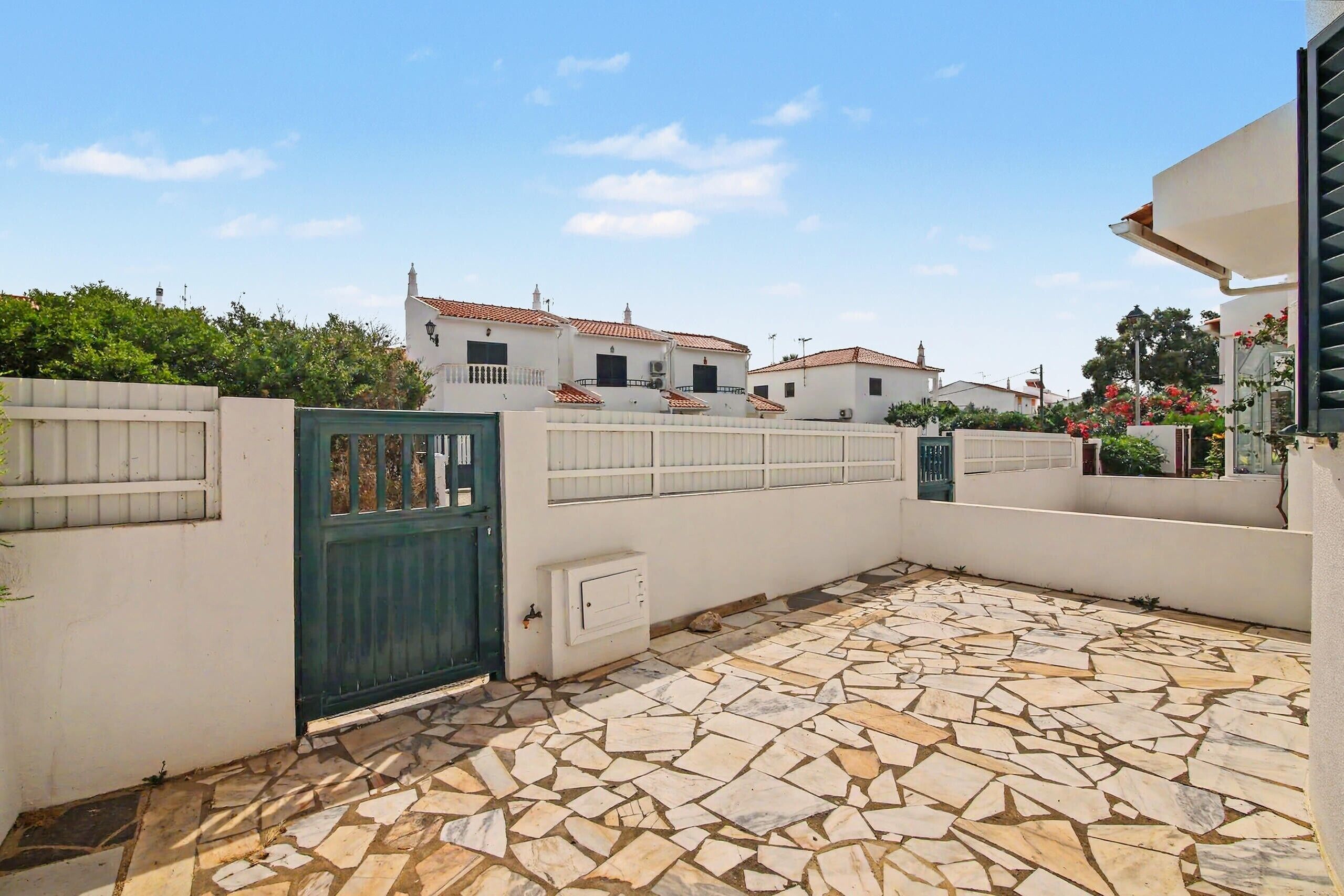 A courtyard with a tiled floor, a green gate, and white buildings in the background.