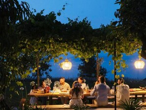 An outdoor dining area with tables and chairs, surrounded by greenery and illuminated by hanging lights. - Villa With Private Pool and Sea View (Briatico)