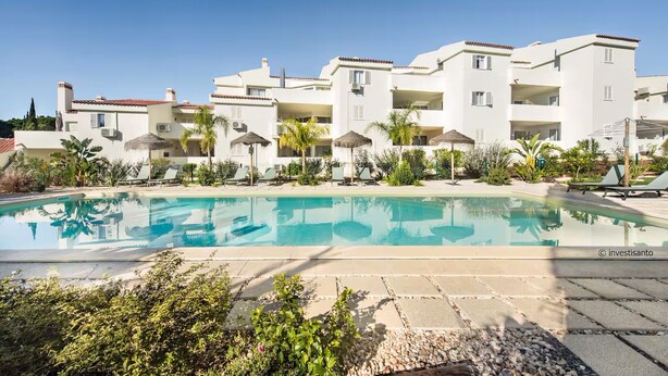 Ein modernes Hotel mit Schwimmbad, mehreren Balkonen und blauem Himmel.