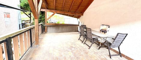 A covered patio with a tiled floor, a table with chairs, and a view of the surrounding area.