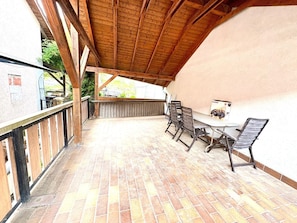 Katettu terassi, jossa on laatoitettu lattia, pöytä ja tuolit sekä näkymä ympäröivään maisemaan.