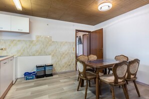 A dining area with a wooden table and chairs, a kitchen with cabinets, and a ceiling with wooden panels.