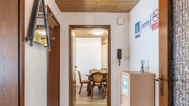 Hotellin käytävä, jossa on puinen katto, vastaanottotiski ja ruokailutila, jossa on tuoleja ja pöytä.