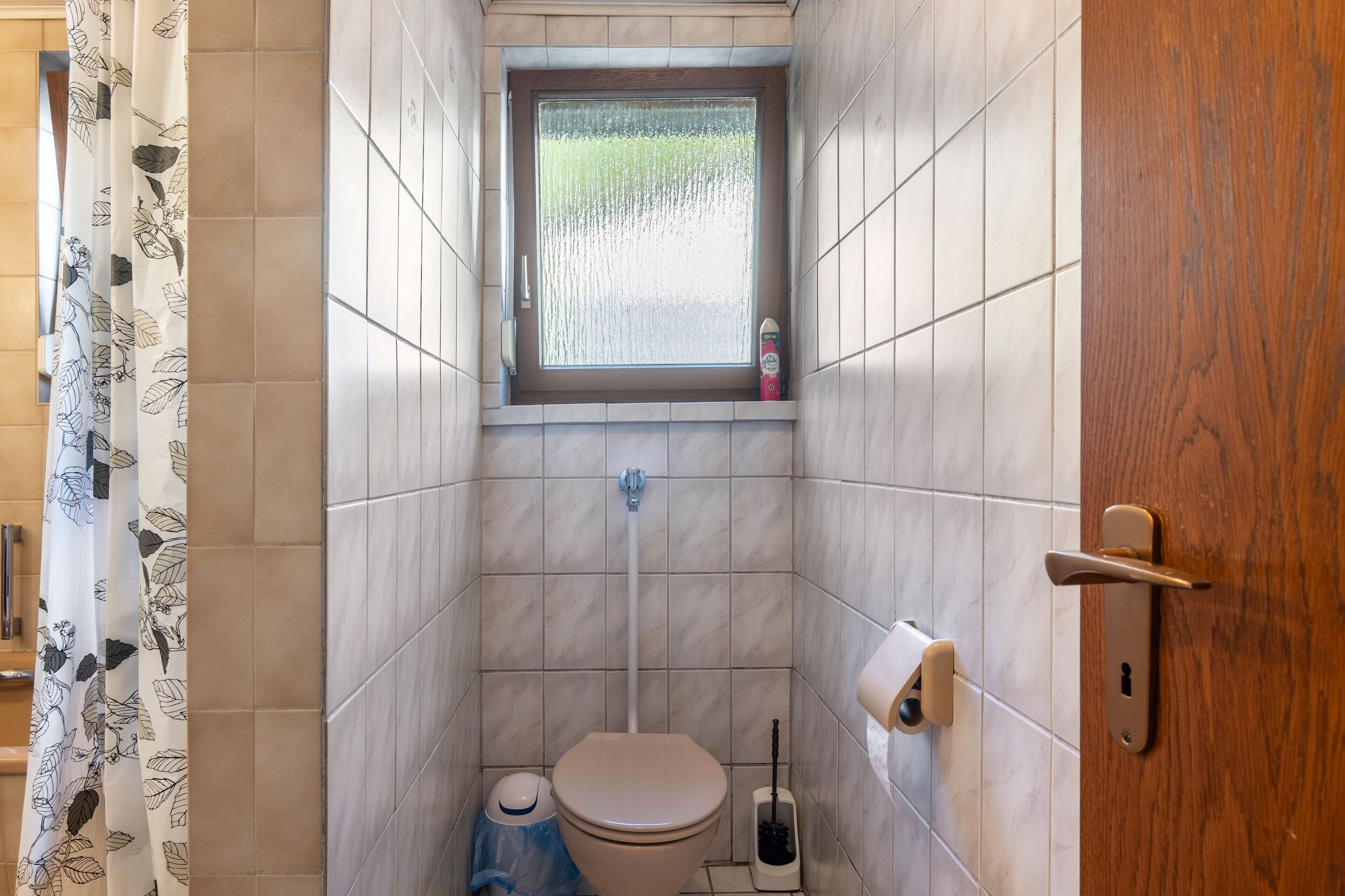 Un baño pequeño con inodoro, ventana, ducha y porta papel higiénico.