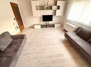 Ein modernes Wohnzimmer mit Flachbildfernseher, integrierten Regalen, zwei Sofas und Holzboden.