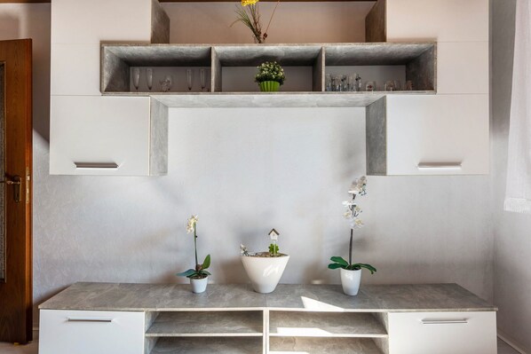 A kitchen with a built-in shelf above the countertop, a white cabinet below, and two potted orchids on the countertop.