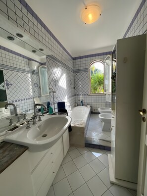 Un baño con un lavamanos grande, una bañera, un inodoro y una ventana que da a zonas verdes.