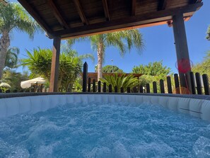 Un jacuzzi bajo una pérgola de madera con palmeras al fondo.