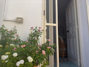 Une porte qui donne sur une pièce contenant un lit et une chaise, un mur blanc et une prise de courant.
